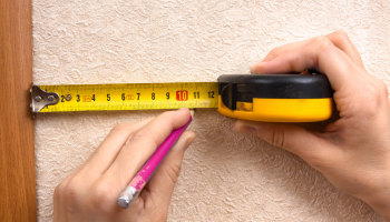 a woman's hands are using a tape measure to mark off a distance on the wall with a pencil