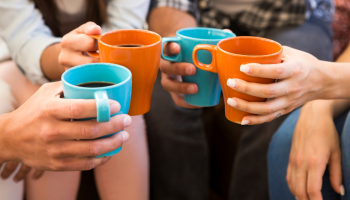 four women are holding mugs (some teal mugs, some orange) and making a toast