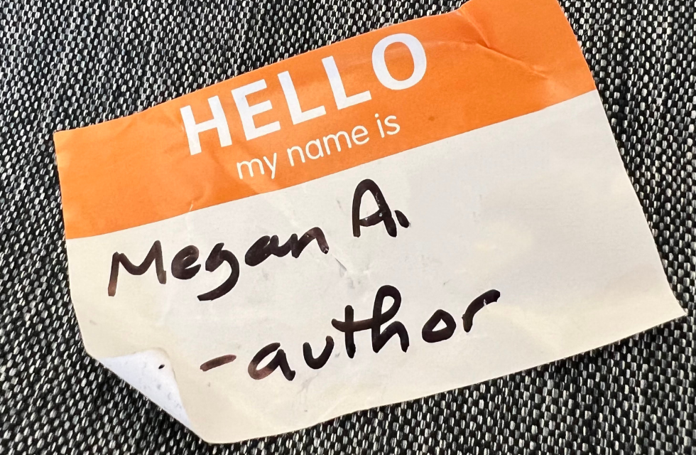 an orange and white adhesive paper nametag that reads "Hello, my name is Megan A. - author"