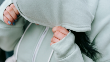 person with long dark hair hiding underneath a green sweatshirt hood