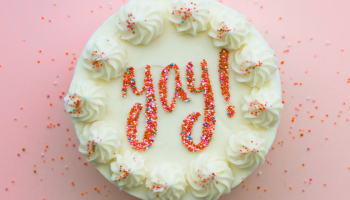 cake with white frosting and coral colored sprinkles that spell out yay!