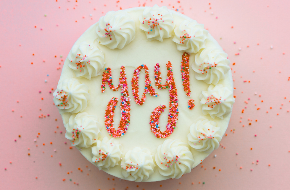 cake with white frosting and coral colored sprinkles that spell out yay!